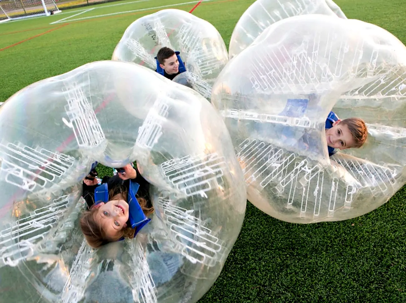 Kids smiling inside clear inflatable bubbles resting on a turf field