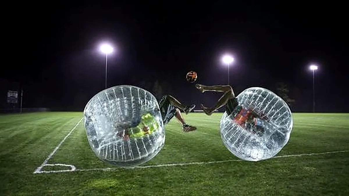 Two players colliding in inflatable bubbles under floodlights at night